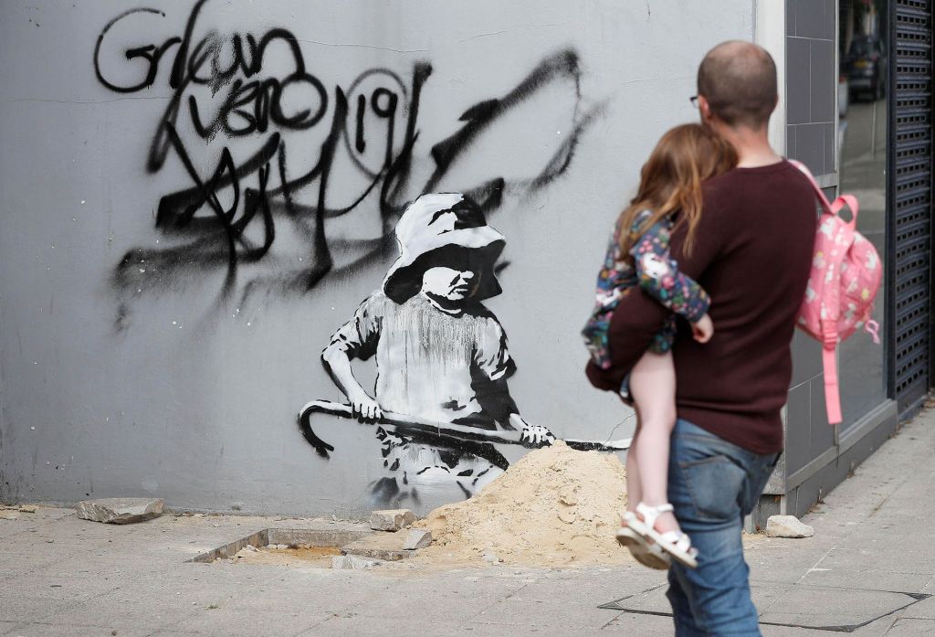 バンクシーの ≪A Great British Spraycation（英国のスプレーケイション）≫作品のひとつを見つめる親子　画像引用：https://www.theartnewspaper.com/